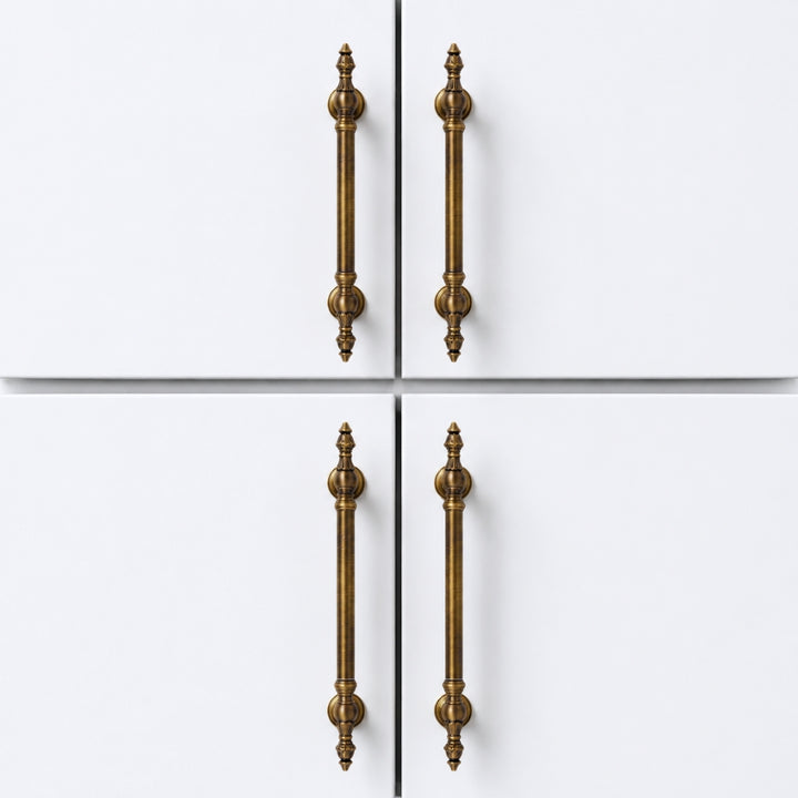 Four long vertical cabinet handles in an antique brass finish, shown on a white four-door cabinet or door front.