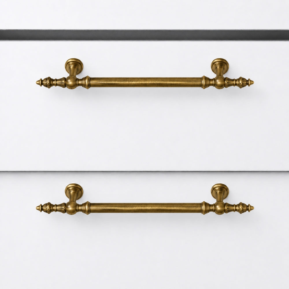 Two matching brass cabinet handles with decorative turned ends and round backplates, shown mounted on white drawer fronts.