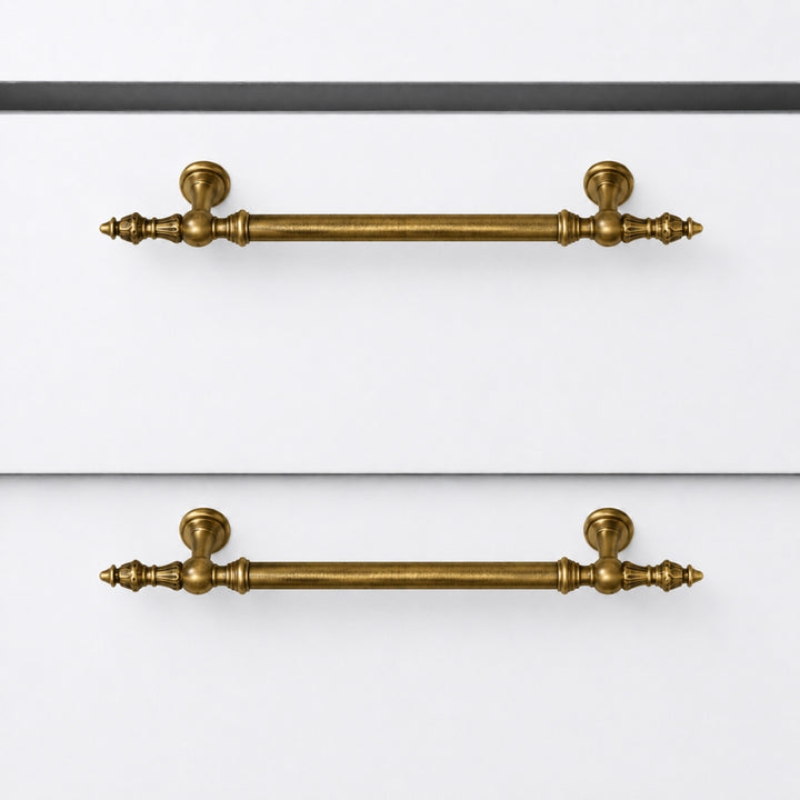 Two matching brass cabinet handles with decorative turned ends and round backplates, shown mounted on white drawer fronts.
