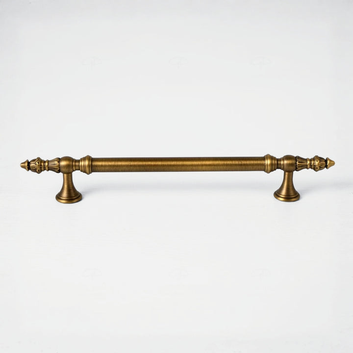 An antique brass cabinet pull handle with ornate turned details and decorative finials on both ends, shown horizontally against a plain white background.
